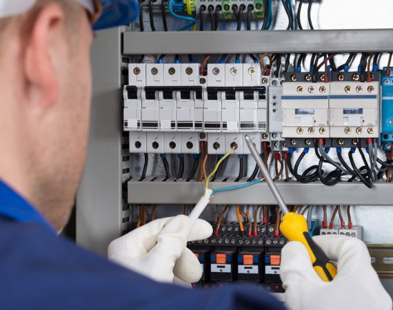 Male Electrician Working On Fusebox With Screwdriver